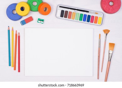 Blank Piece Of Paper With Colorful Pencils, Brushes And Watercolors On Kid's Desk, Top View With Copy Space