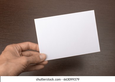 Blank Postcard In Hand On Wooden Background. Leaflet A6 Mockup