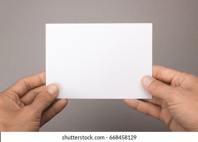 Blank Postcard In Hands On A Gray Background. Leaflet A6 Mockup