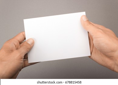 Blank postcard in hands on a gray background. Leaflet A6 mockup