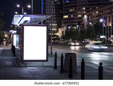 Blank Poster On Bus Stop At Night. Copy Space. In Background Out Of Focus Street, Cars, Buildings.