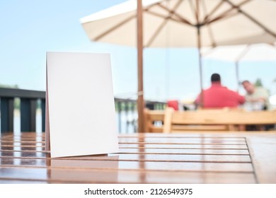 Blank poster on a table on the terrace of a restaurant, outdoors, in summer. White space to display a text, menu, products, promotions or other information to customers. - Shutterstock ID 2126549375