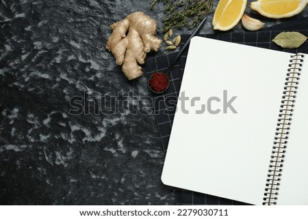 Blank recipe book and different ingredients on black textured table, flat lay. Space for text