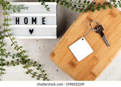 Blank rhombus white sublimation keychain mockup next to board with home inscription. Key chain mockup to display design.