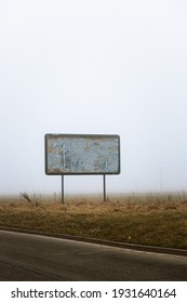 Blank Ripped Billboard On The Edge Of The Road On The Field That Has Apocalyptic Vibe, Because Of The Mist And Moody Background.