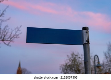 Blank road sign on a post. Template for the name of a street in front of an evening sky. Mockup of a metal plate showing information for traffic in Germany.