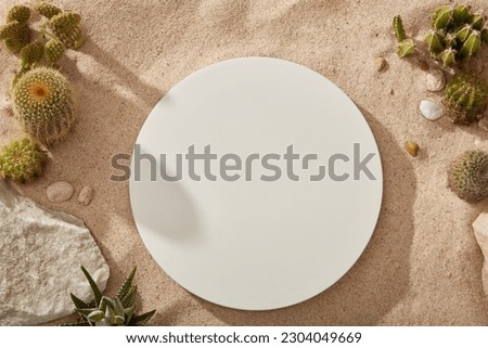 Blank round podium in white color decorated on sand background. Decorated with a block of stone, gravels and several types of Cactus