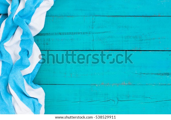 Blank rustic teal blue wood beach sign with turquoise\
and white striped beach towel border; blue painted background with\
copy space 