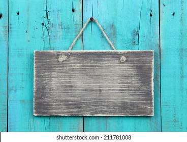 Blank rustic wood sign hanging on antique teal blue wooden background; distressed background with copy space