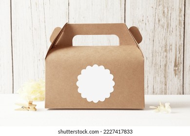 Blank scallop sticker on a kraft favor box with beige flower and wooden clip on a white wood background. White sticker mockup, wedding,party sticker, logo sticker. Branding, white copy space. - Shutterstock ID 2227417833