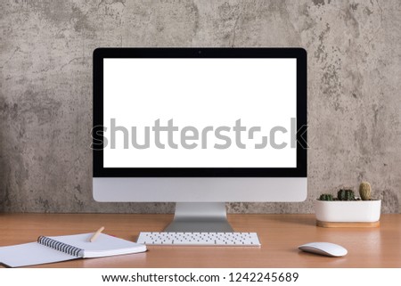 Blank screen of all in one computer with note book, pencil and cactus vase on raw concreate background