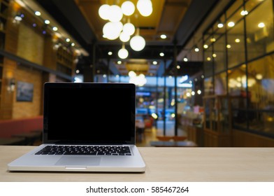 Blank Screen Display Laptop On Wooden Table With Blurred Background Of Coffee Shop With Empty People For Co Work Space; Out Side Office Conceptual