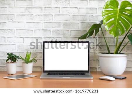 Blank screen of Laptop computer with tablet, mobile phone, mouse and monstera plant pots on wooden table, White background