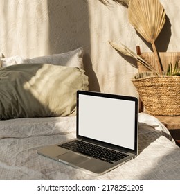 Blank Screen Laptop. Sunlight Shadows On The Wall. Parisian Vibes. Warm Bohemian Style Home Interior Design. Copy Space Mockup Template. Hygge Bedroom With Bed, Pillows, Linens, Decorations.