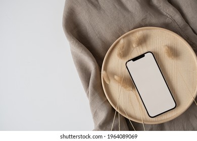 Blank Screen Mobile Phone, Rabbit Tail Grass On Wooden Tray With Crumpled Linen Cloth Blanket. Flat Lay, Top View Minimalist Blog, Website, App Template. Copy Space Mockup.