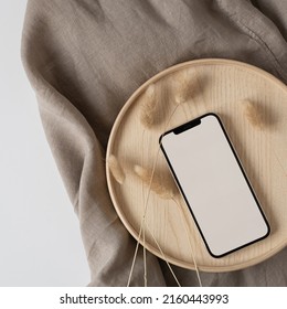 Blank Screen Mobile Phone, Rabbit Tail Grass On Wooden Tray With Crumpled Linen Cloth Blanket. Flat Lay, Top View Minimalist Blog, Website, App Template. Copy Space Mockup.