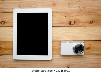 Blank screen of tablet computer with digital camera on wooden background