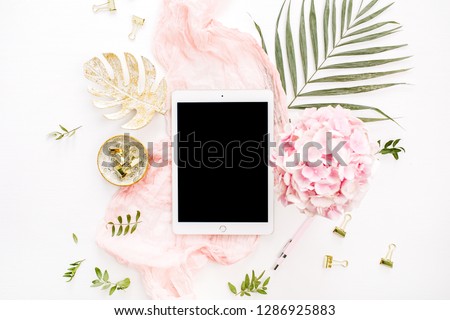 Blank screen tablet, pink hydrangea flowers bouquet, tropical palm leaf, pastel blanket, monstera leaf plate and accessories on white background. Flat lay, top view rose gold home office desk.