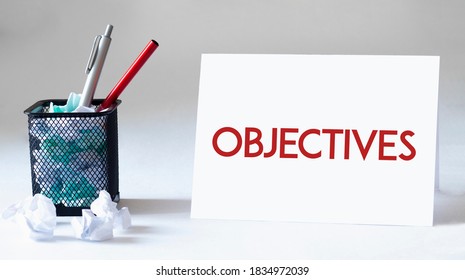 Blank sheet, pen and crumpled paper balls on grey table, flat lay. Text OBJECTIVES