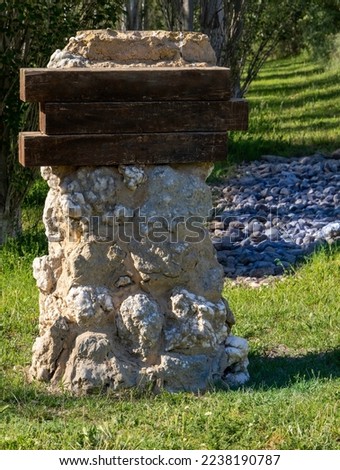 Blank signpost in a poplar forest. Wooden sign on stone milestone. Sunny day