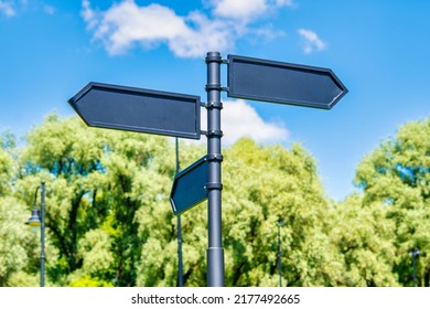 Blank signs with directions in the park. Black arrows against the sky and green trees. - Powered by Shutterstock