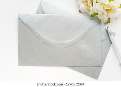 Blank Silver Envelopes For Design, Address Label Or Sticker Presentation, Wedding Envelope Mockup, White Flowers, Pen, Top View.