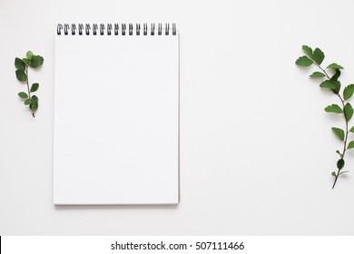 Blank sketchbook on white background, free space. Top view on empty rustic style notepad with green leaves on table, copy space for text or advertisement
