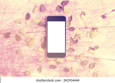 Blank smartphone on wooden table with leaves, mock up, instagram photo effect