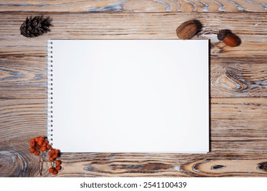  A blank spiral notebook on a rustic wooden surface, surrounded by autumn-inspired decor including red berries, acorns, and a pine cone, offering a cozy seasonal setting for creative projects. - Powered by Shutterstock