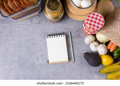 Blank spiral notepad with a pencil beside it surrounded by a lot of prepared food inside glass jars over a kitchen table. Horizontal photo. - Shutterstock ID 2146446173