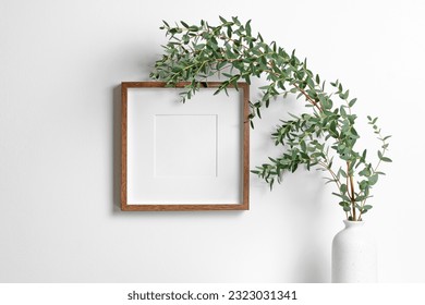 Blank square frame mockup for artwork or print on white wall with eucalyptus plant in vase, frame with copy space