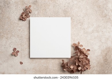 Blank square paper card mockup with copy space for card design on beige background with botanical decor, top view