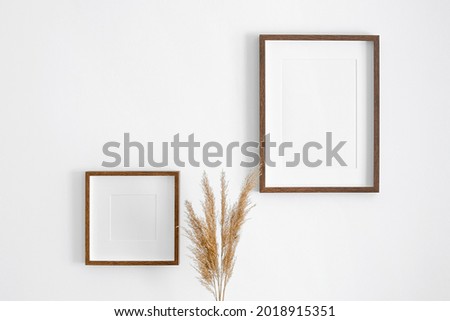 Blank square and portrait frames mockup on white wall with dry plant decorations. Minimalistics style interior with artwork mockup.