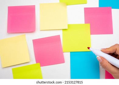 Blank Sticker Notes On White Background. Hand With Red Marker Ready To Write. Mockup Sticky Note Paper. Empty Sheets For Notes On White Bulletin Board. Colored Sticky Notes