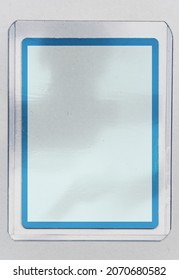 Blank Trading Card With Blue Border Behind Transparent Plastic Top Loader Case On White Paper Background.