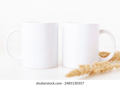 Blank two white coffee mugs on table with dried flowers. 11 oz ceramic cups mockup template in boho style.