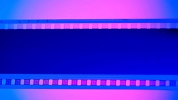 Blank Undeveloped Strip Of Film On Blue Background, Illuminated By Pink Neon Light In Close Up. 35mm Film Slide Frame. Cinema Or Photo Frames. Long, Retro Film Strip Frame. Copy Space.