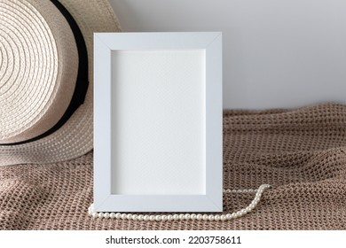 Blank Vertical White Frame Beside A Beach Hat For Artwork Display On Brown Knitted Cloth For Summer Trip Memorial.