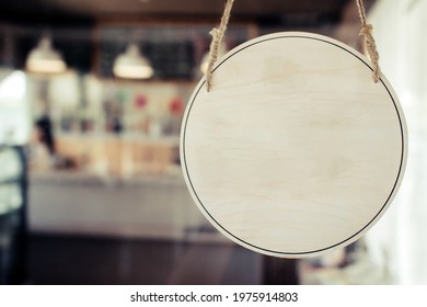 blank vintage wooden sign board hanging on glass door in modern cafe restaurant, copy space for text advertising, advertisement marketing and small business owner concept