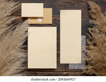 Blank Wedding Cards And Envelope On Dark Brown Wood Near Pampas Grass Top View. Boho Rustic Scene With Wedding Cards Set Mockup, Flat Lay. 