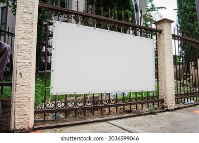 Blank White Advert Banner With Mockup Space Hanging On Metal Fence Over Street Sidewalk