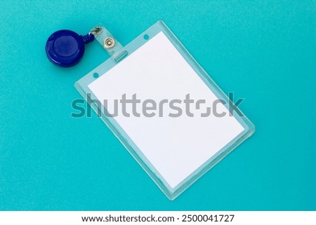 The blank white badge, attached to a blue lanyard reel, represents personal identification and access control. The turquoise background adds a modern touch, making this image suitable for corporate se