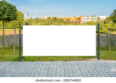 Blank white banner for advertisement on the fence. Residential area with modern buildings and tower crane in the background.