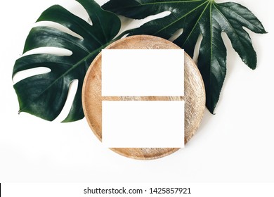 Blank white business cards mockups, wooden plate, aralia and monstera leaf isolated on white table backgound. Modern template for branding identity. Tropical design. Wedding stationery. Flat lay, top 