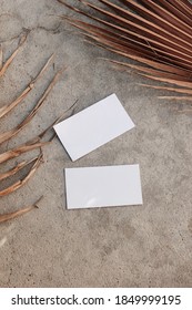 Blank white business cards mockups and dry brown palm leaves on textured table backgound. Elegant modern template for branding identity. Tropical design. Wedding stationery. Flat lay, top view.