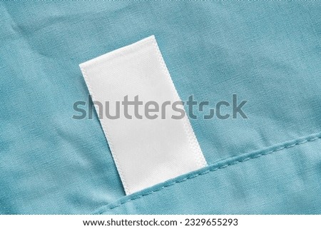 Blank white clothes label sewn on blue cotton fabric background
