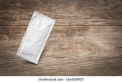 Blank White Condiment Packet Floating On Aged Wood Background.