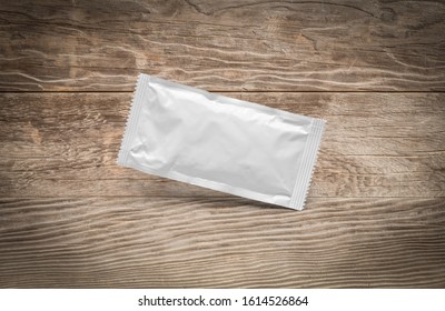 Blank White Condiment Packet Floating On Aged Wood Background.