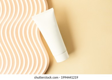 Blank white cosmetics tube on the beige background.Wavy podium near it.Good as cosmetic mockup,pastel banner with copy space.