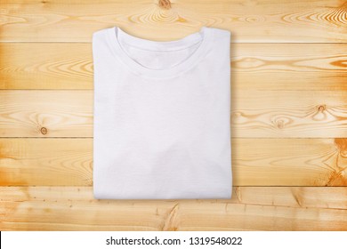 Blank White Folded T-shirt On Wooden Background. Plain White Tshirt On Natural Wooden Texture. Flat Lay. Top View